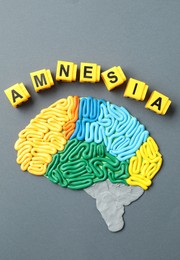 Photo of Word Amnesia and brain with sections made of plasticine on grey background, flat lay