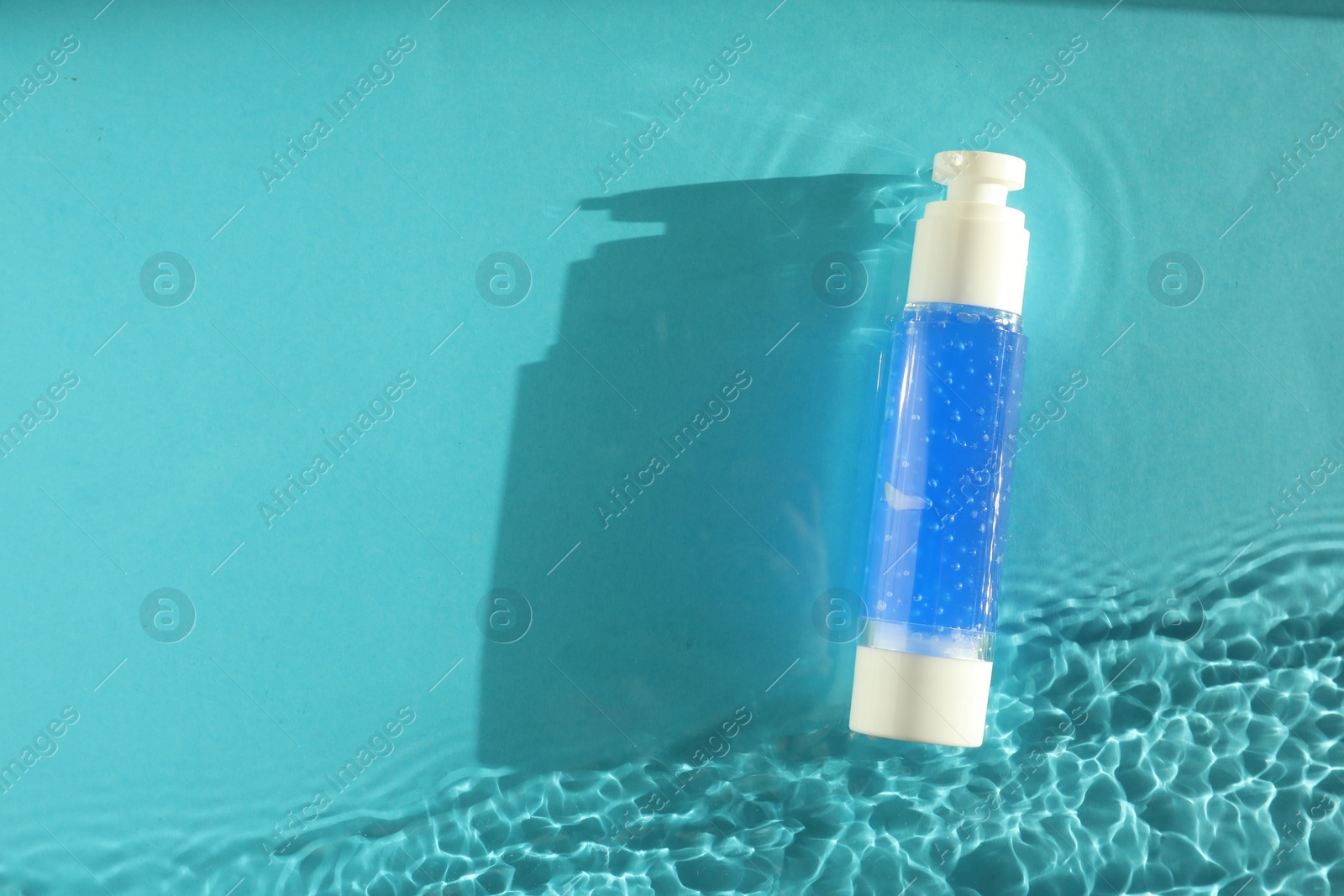 Photo of Bottle of cosmetic product in water on turquoise background, top view. Space for text