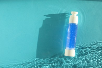 Photo of Bottle of cosmetic product in water on turquoise background, top view. Space for text