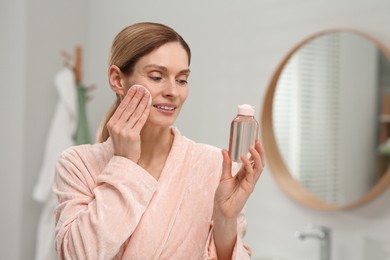 Photo of Beautiful woman removing makeup with cotton pad indoors, space for text