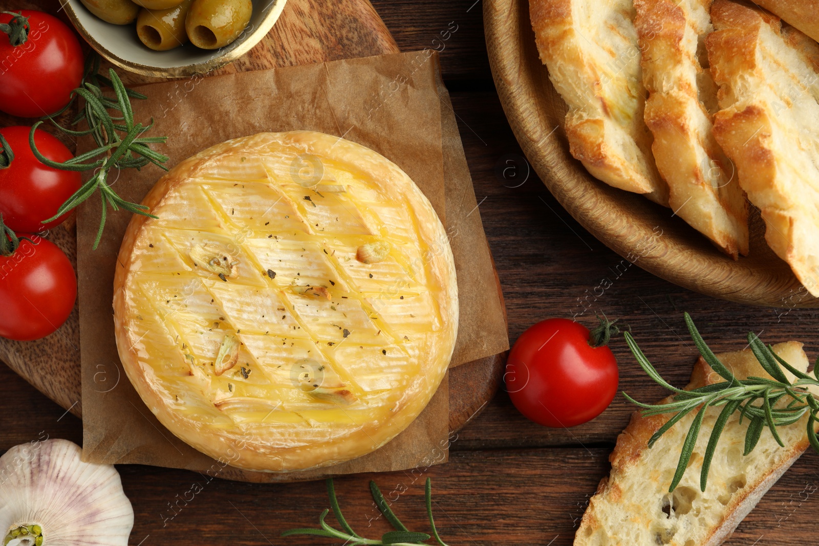 Photo of Tasty baked brie cheese served on wooden table, flat lay