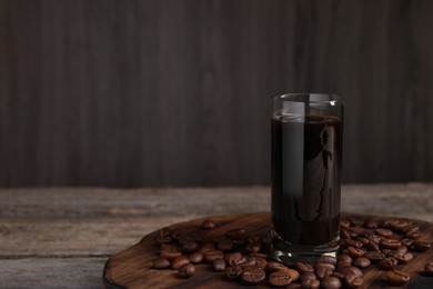 Glass of coffee liqueur and beans on wooden table, space for text