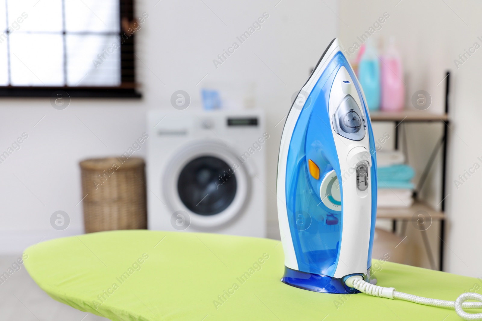 Photo of Modern clothes iron on board in laundry room