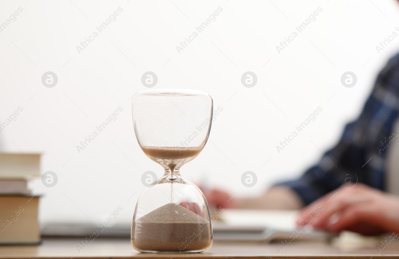 Photo of Hourglass with flowing sand on desk. Man taking notes indoors, selective focus