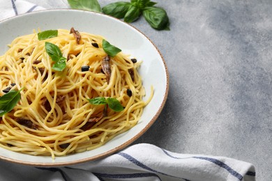 Photo of Delicious pasta with anchovies, olives and basil on light grey table. Space for text
