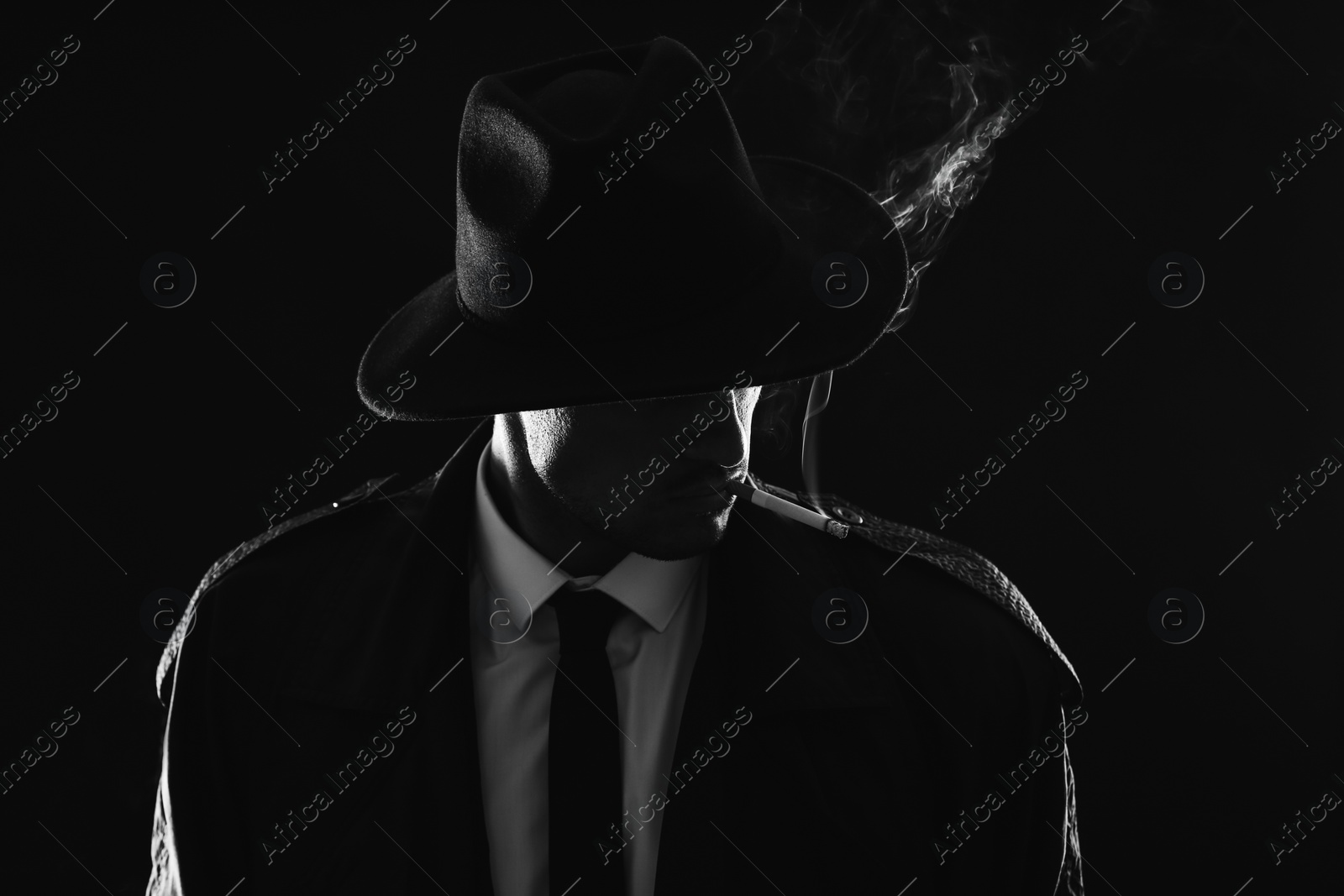 Photo of Old fashioned detective smoking cigarette on dark background, black and white effect