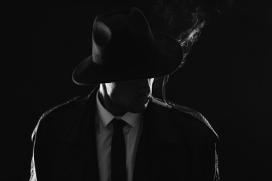 Photo of Old fashioned detective smoking cigarette on dark background, black and white effect