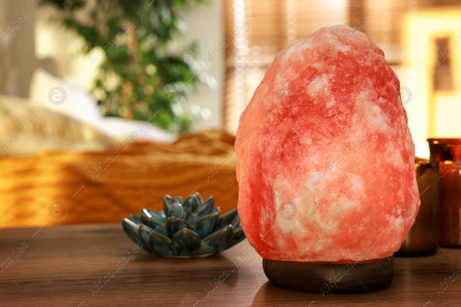 Photo of Beautiful Himalayan salt lamp, lotus figure and candles on wooden table in bedroom, space for text