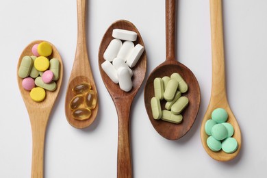 Photo of Different vitamin pills in wooden spoons on white background, flat lay