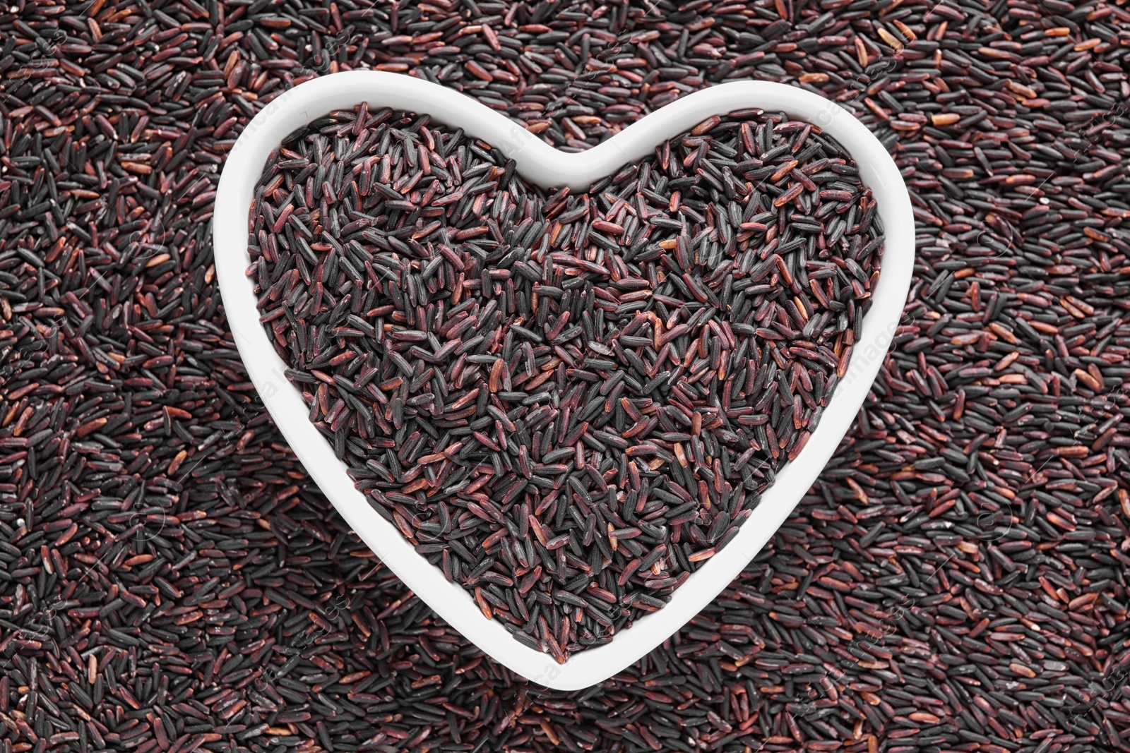 Photo of Pile of brown rice with heart shaped bowl, top view