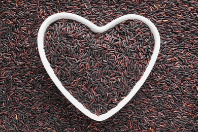 Pile of brown rice with heart shaped bowl, top view