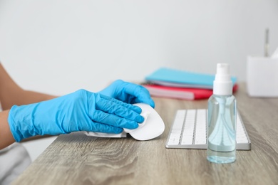 Photo of Woman cleaning computer mouse with antiseptic wipe in office, closeup