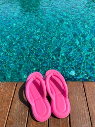 Clear rippled water in swimming pool and pink flip-flops on wooden deck outdoors. Space for text