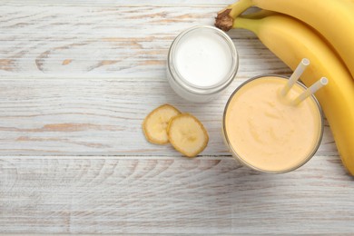 Photo of Glass of tasty banana smoothie with straws and ingredients on white wooden table, flat lay. Space for text