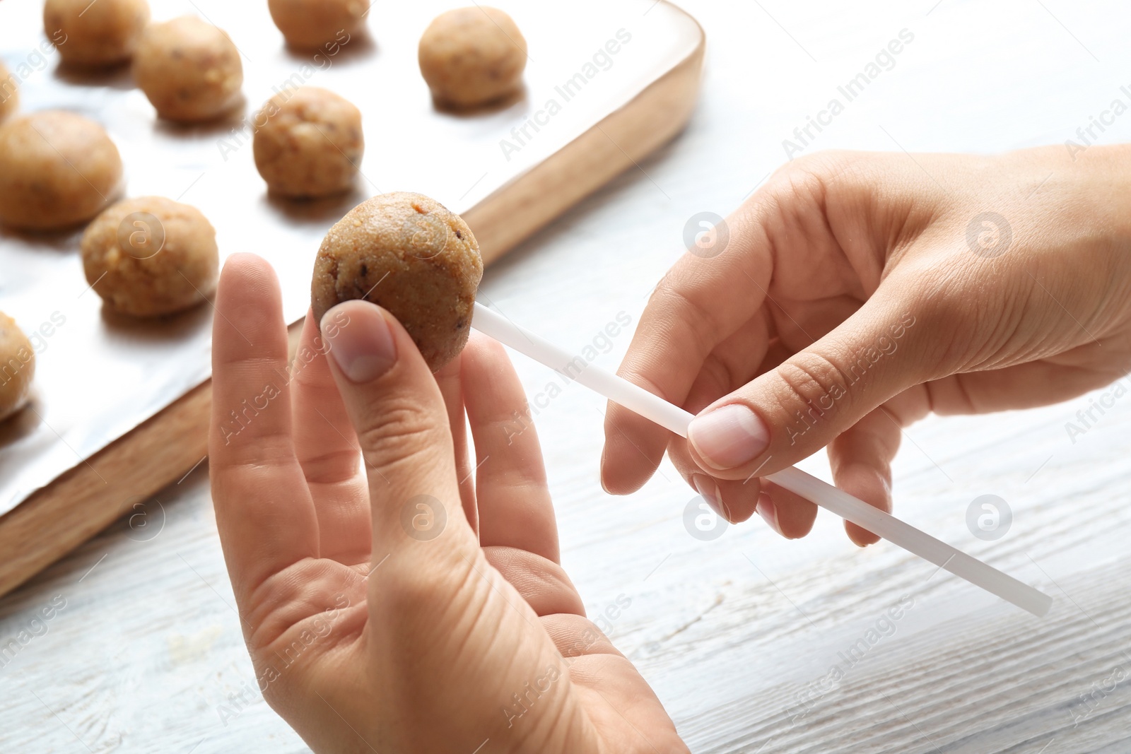 Photo of Woman making tasty cake pops at white wooden table, closeup