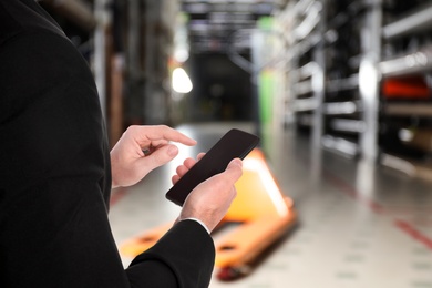 Image of Wholesale trading. Man using WMS app on smartphone at warehouse, closeup 