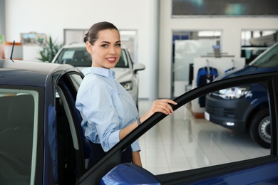 Young saleswoman near automobile in car dealership