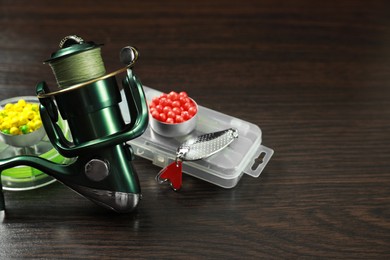 Photo of Fishing tackle. Spinning reel, baits and lure on dark wooden background, closeup. Space for text