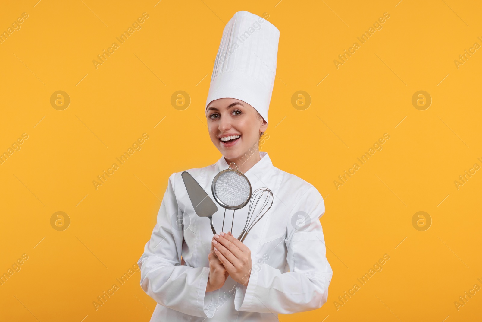 Photo of Happy confectioner in uniform holding professional tools on yellow background