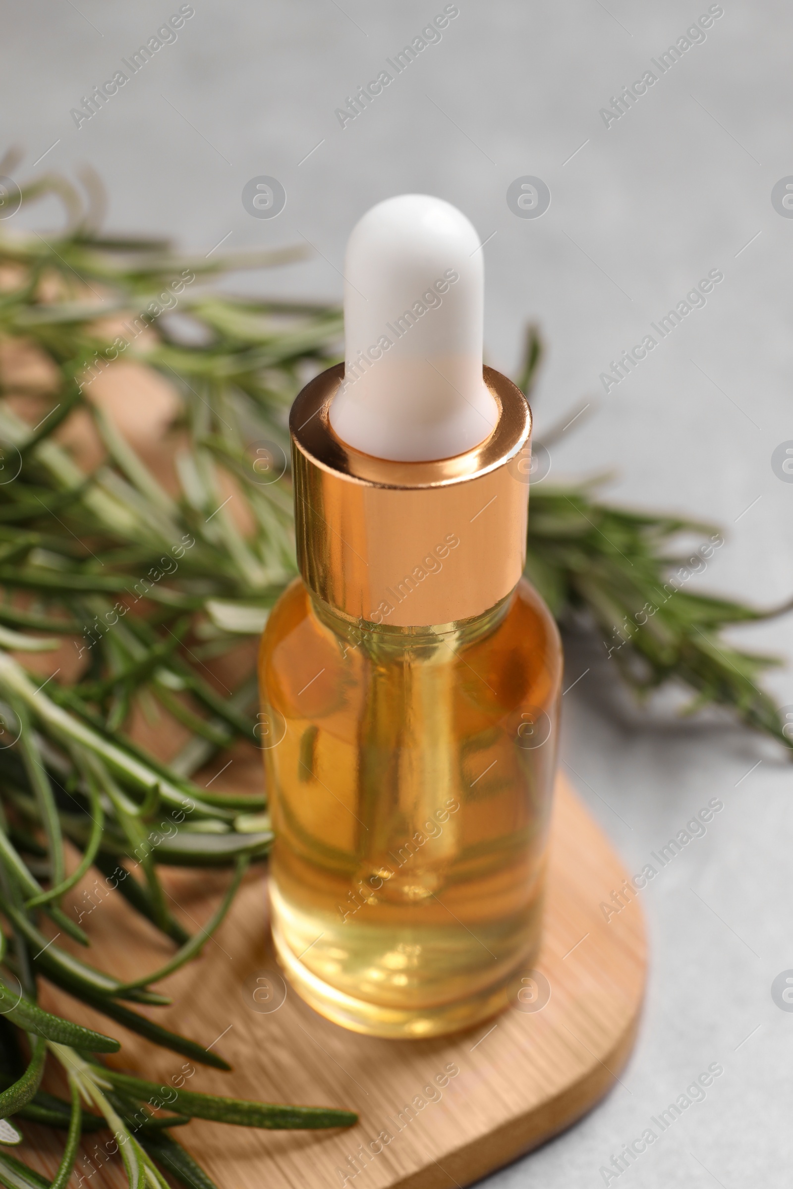 Photo of Bottle of essential oil and fresh rosemary on light grey table, closeup