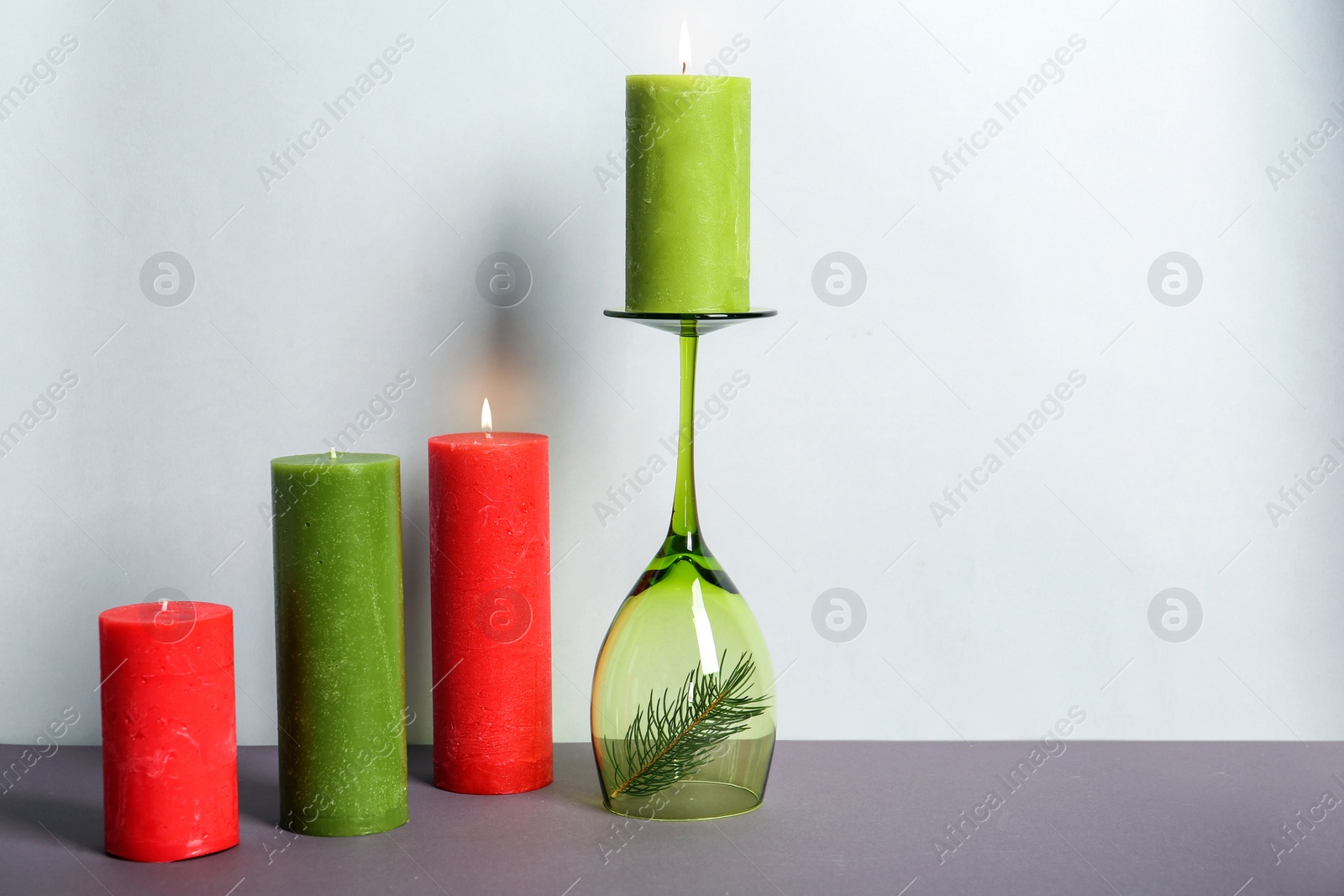 Photo of Decorative wax candles and wineglass on table against light background