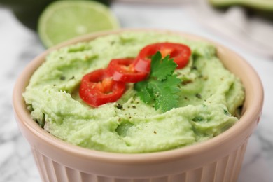 Photo of Bowl of delicious guacamole with chili pepper on white table, closeup