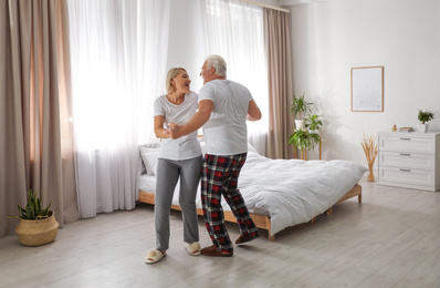 Happy mature couple dancing together in bedroom