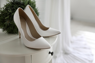 Photo of Pair of white high heel shoes, wreath and blurred wedding dress on background, space for text