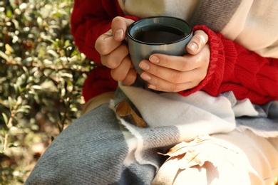 Woman in cozy sweater with cup of hot drink outdoors on sunny autumn day, closeup