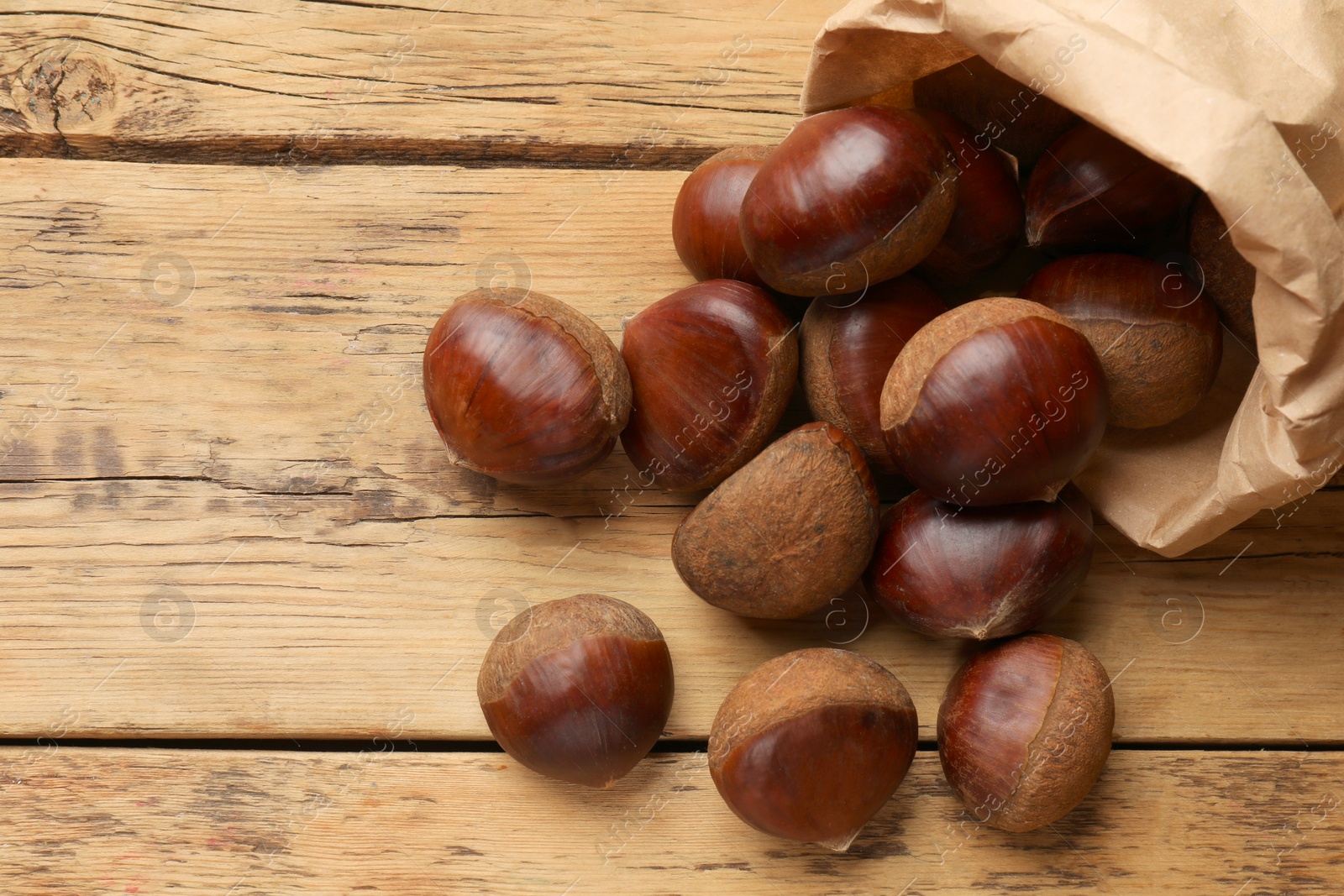 Photo of Sweet fresh edible chestnuts in paper bag on wooden table, top view. Space for text