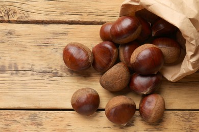 Photo of Sweet fresh edible chestnuts in paper bag on wooden table, top view. Space for text