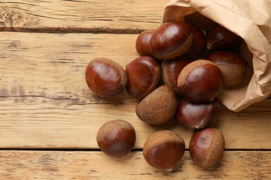 Sweet fresh edible chestnuts in paper bag on wooden table, top view. Space for text