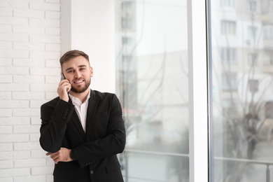 Young businessman talking on phone near window at home