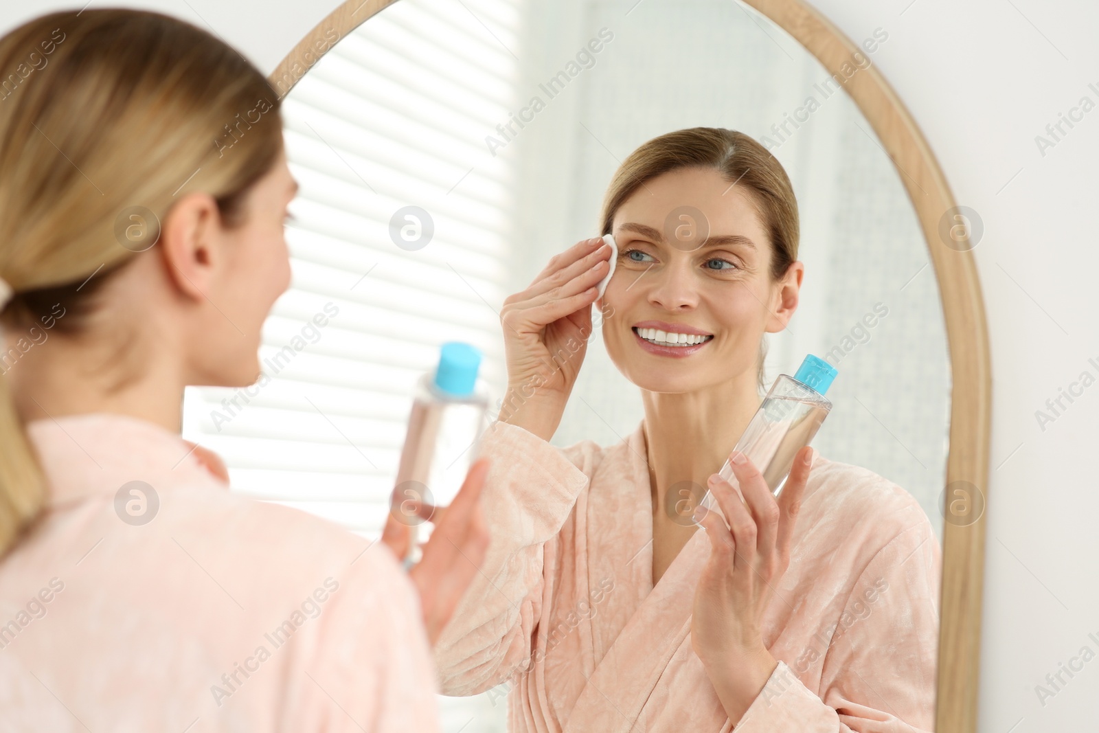 Photo of Beautiful woman removing makeup with cotton pad near mirror indoors