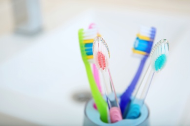 Photo of Cup with different toothbrushes near sink, closeup. Dental care