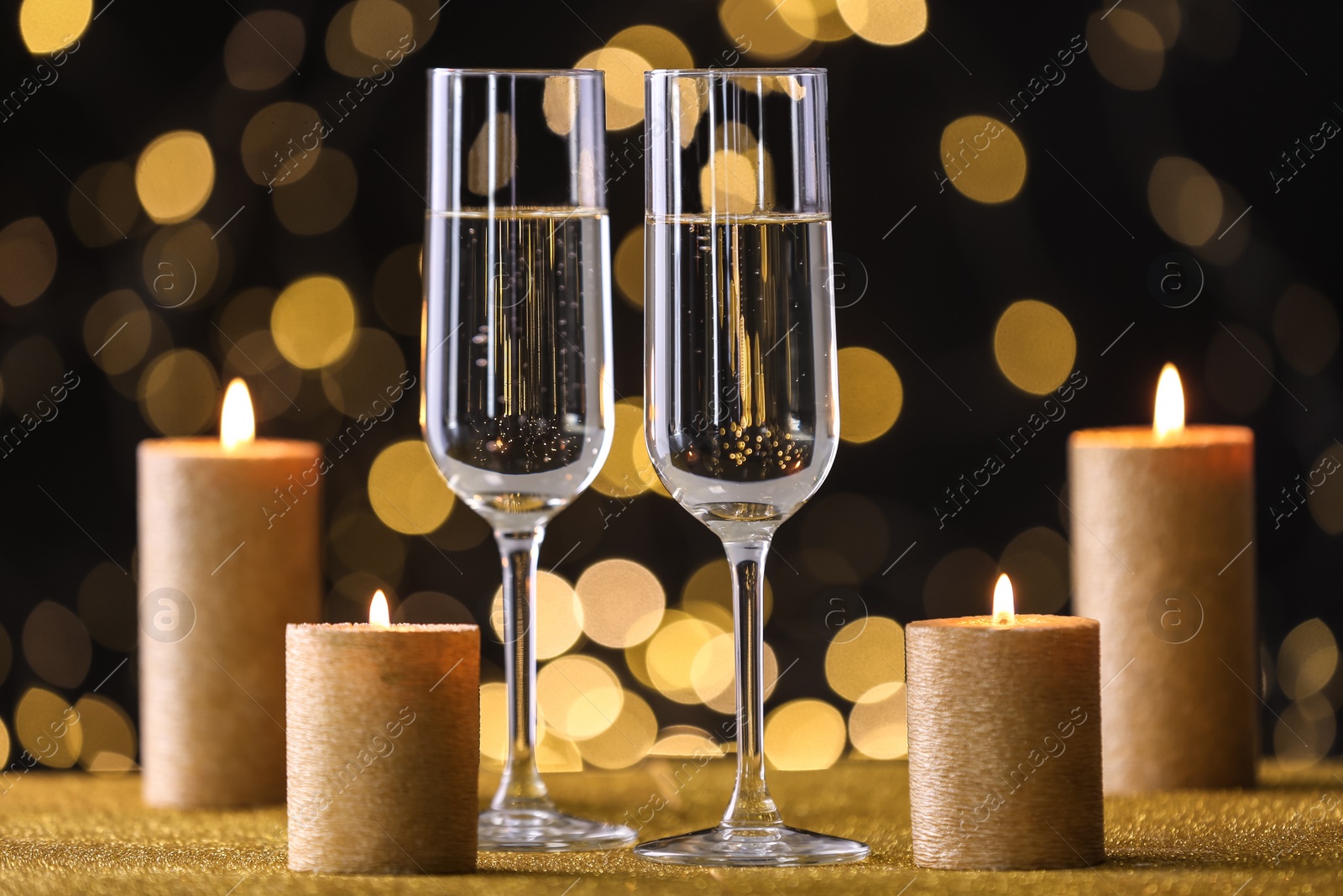 Photo of Champagne glasses and golden candles on table against defocused lights