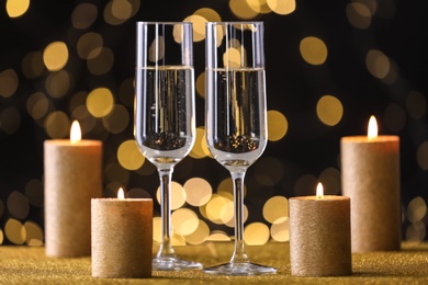 Champagne glasses and golden candles on table against defocused lights