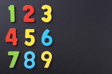 Colorful numbers on black background, flat lay. Space for text