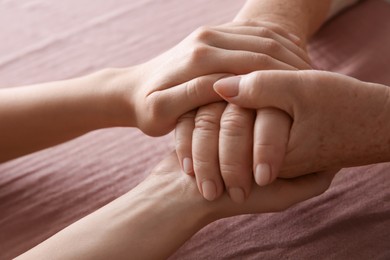 Photo of Young and elderly women holding hands together on pink fabric, closeup