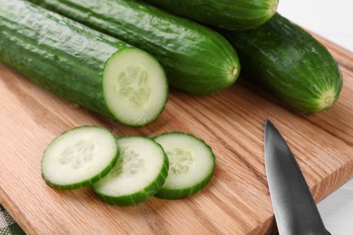 Fresh cucumbers and knife on wooden cutting board, closeup