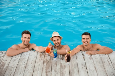 Photo of Happy young friends with refreshing cocktails in swimming pool