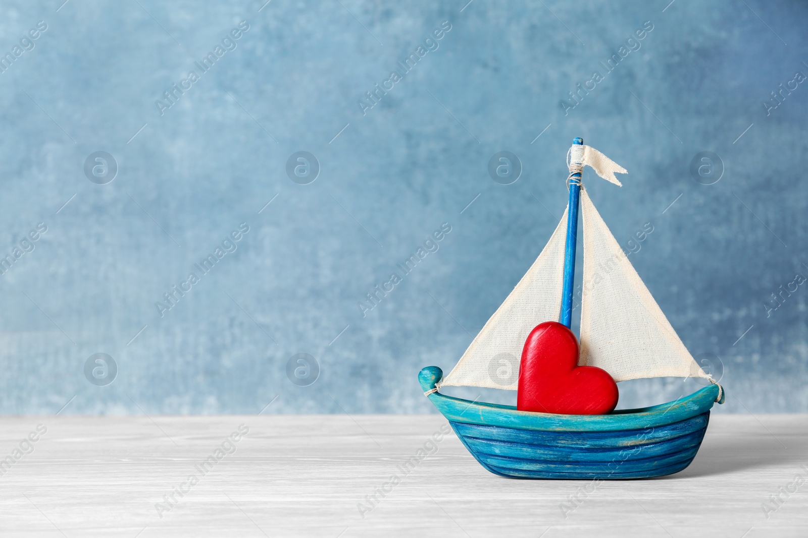 Photo of Toy ship with red decorative heart on table. Space for text