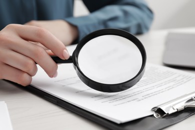 Photo of Woman looking at document through magnifier at white wooden table, closeup. Searching concept