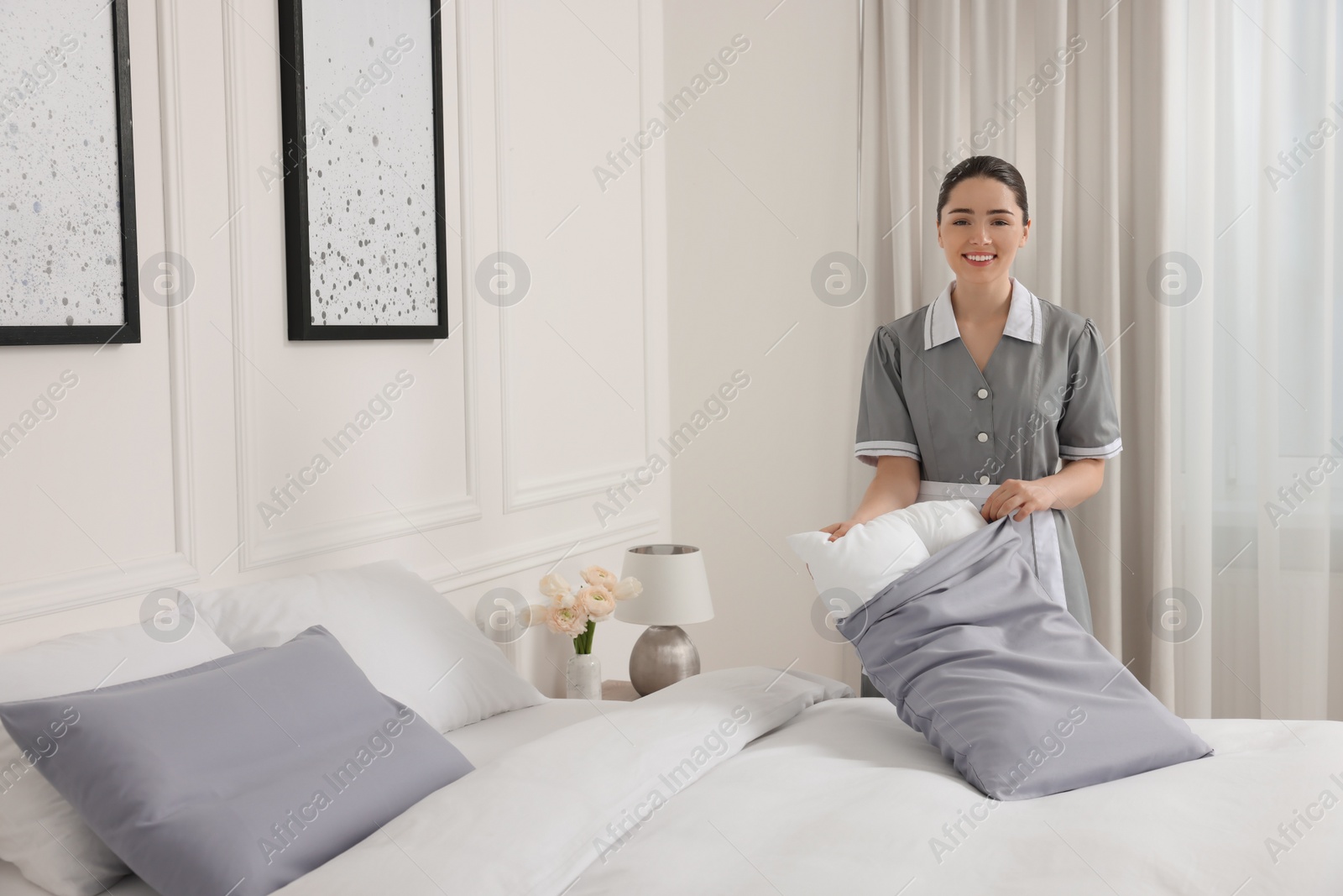 Photo of Young maid making bed in hotel room. Space for text