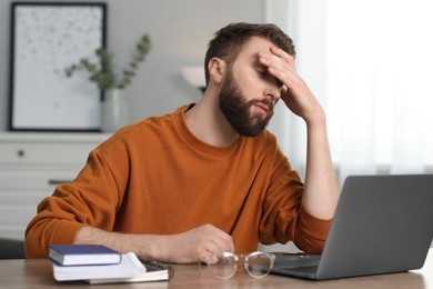 Photo of Overwhelmed man sitting with laptop at table indoors