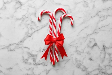 Photo of Candy canes with bow on white marble background, top view. Traditional Christmas treat