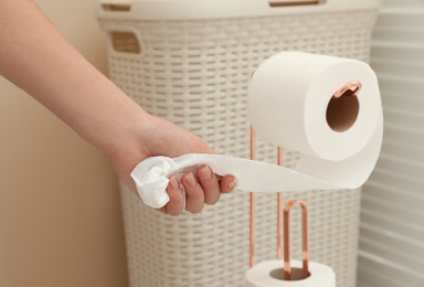 Photo of Woman taking toilet paper from roll holder in bathroom, closeup