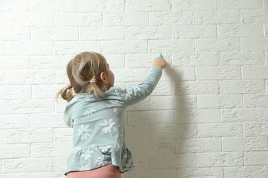 Little girl drawing on white brick wall, back view and space for text. Child`s art