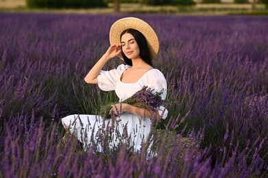 Photo of Beautiful young woman with bouquet sitting in lavender field