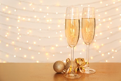 Photo of Glasses of champagne and Christmas balls on table against blurred lights